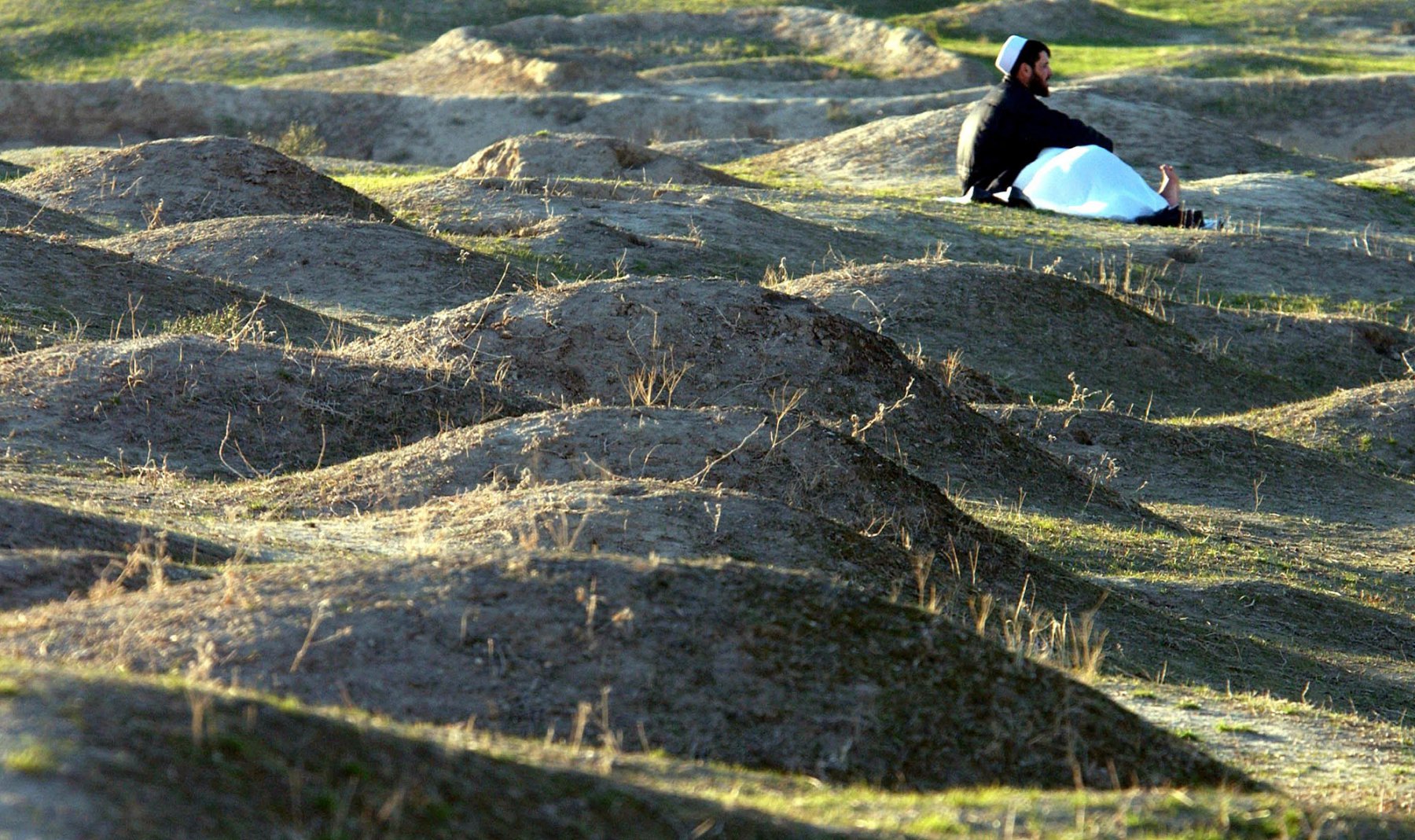 An Afghan man sits lonely between the graves on the central cemetery in Kundus, Afghanistan. Photo: Boris Roessler/dpa