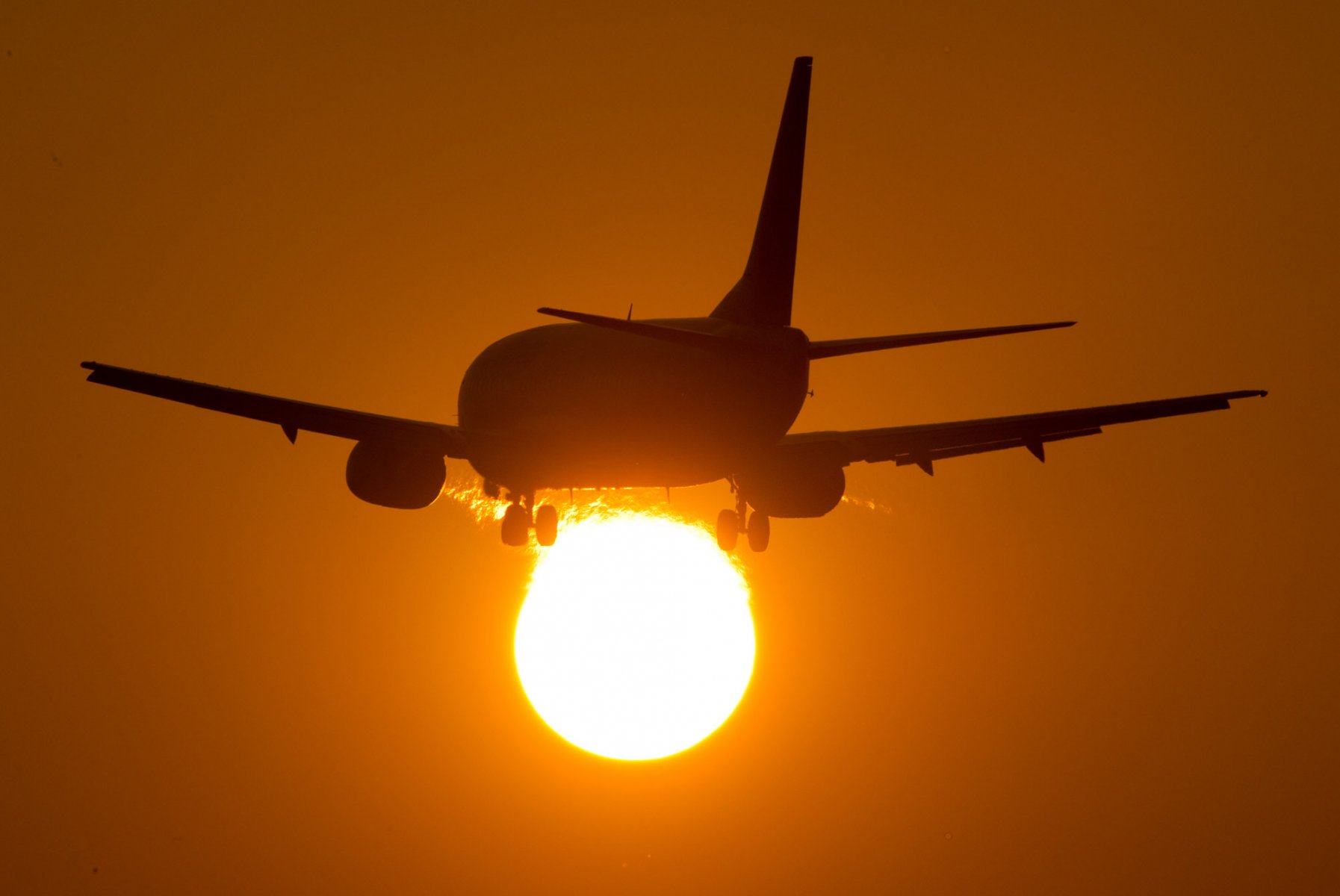 Als dunkler Schatten hebt sich eine landende Passagiermaschine auf dem Flughafen Frankfurt gegen die untergehende Sonne ab. Foto: Boris Roessler/dpa 
