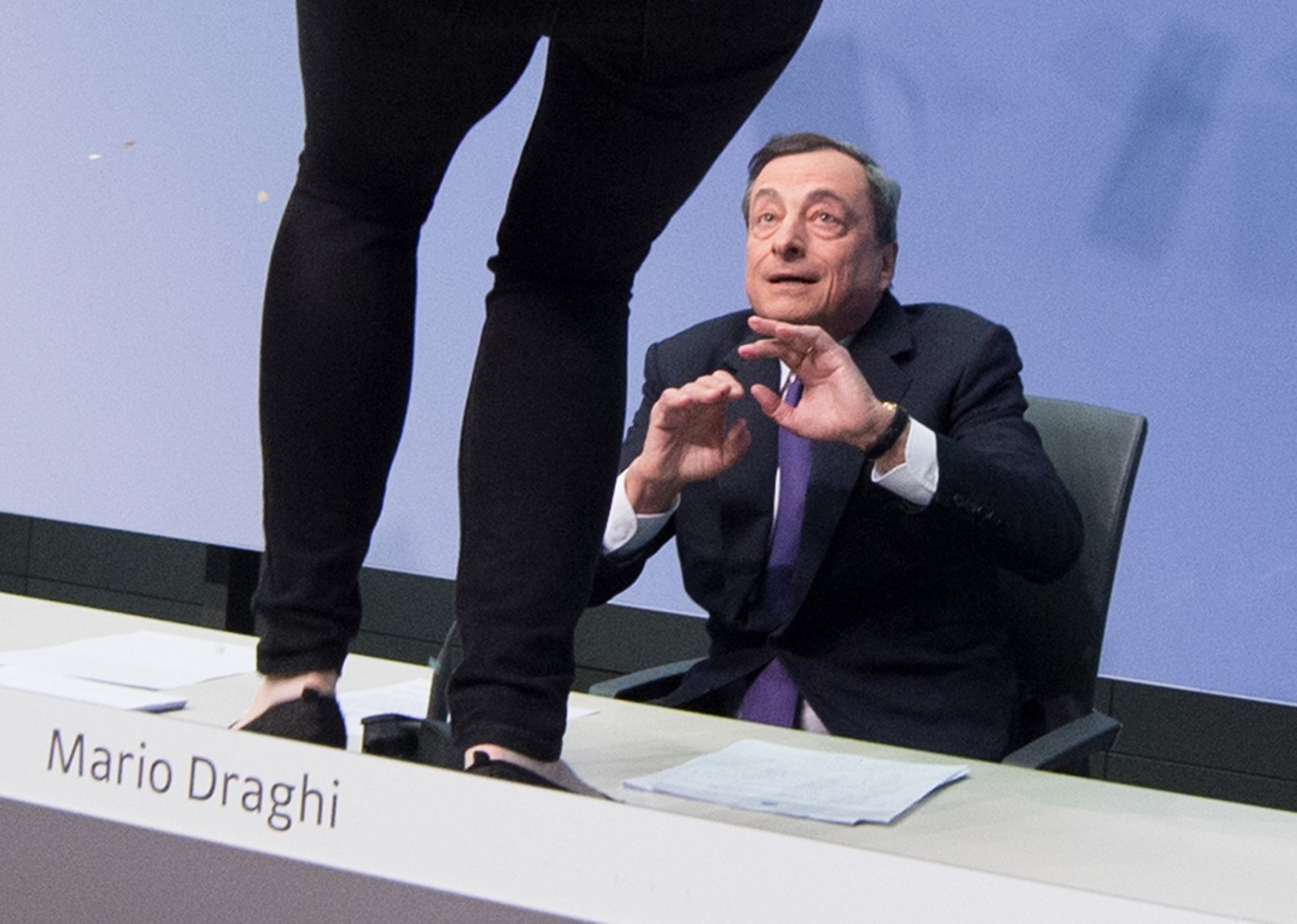 Eine Aktivistin stört die Pressekonferenz der Europäischen Zentralbank in Frankfurt am Main (Hessen) und steht dabei vor dem  EZB-Präsidenten Mario Draghi auf einem Tisch. Foto: Boris Roessler/dpa 