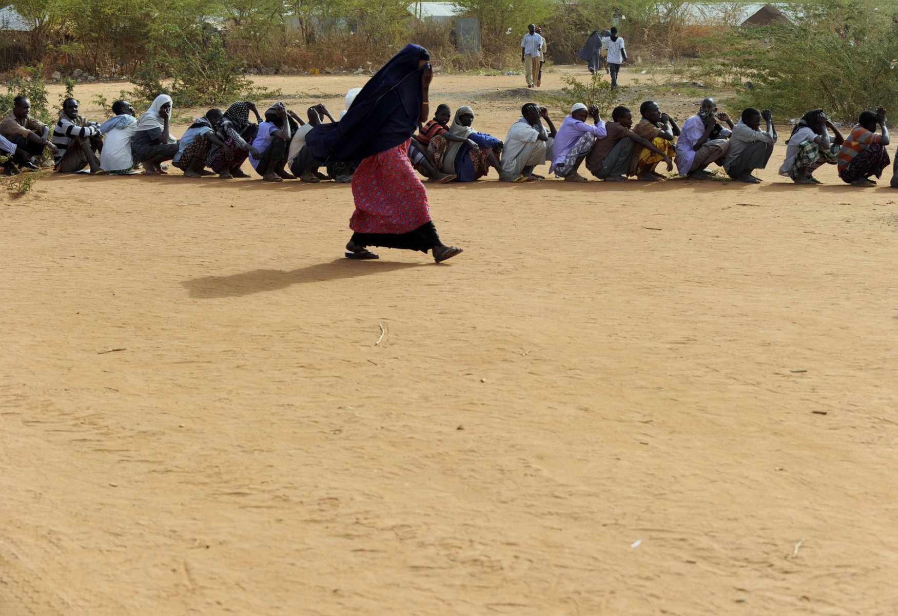 A woman passes by refugees who have lined up outside a refugee camp in Dadaab, northeastern Kenya Friday, August 5, 2011. Somalia and parts of Kenya have been struck by one of the worst droughts and famines in six decades, more than 350.000 refugees have found shelter in the world's biggest refugee camp. Foto: Boris Roessler dpa  +++(c) dpa - Bildfunk+++