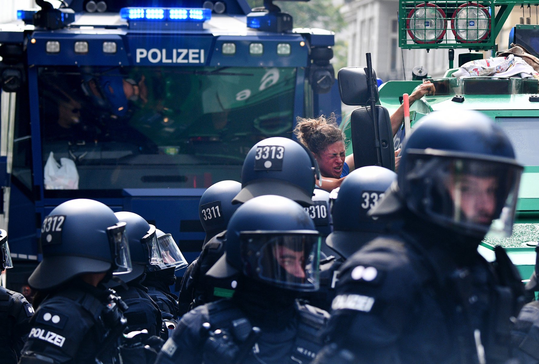 Nachdem sie auf einen Sonderwagen der Polizei geklettert war und von Beamten mit Tränengas besprüht worden war, wird eine junge Demonstrantin beim G-20 in Hamburg von Beamten von dem Fahrzeug geholt, während im Hintergrund Wasserwerfer bereit stehen.