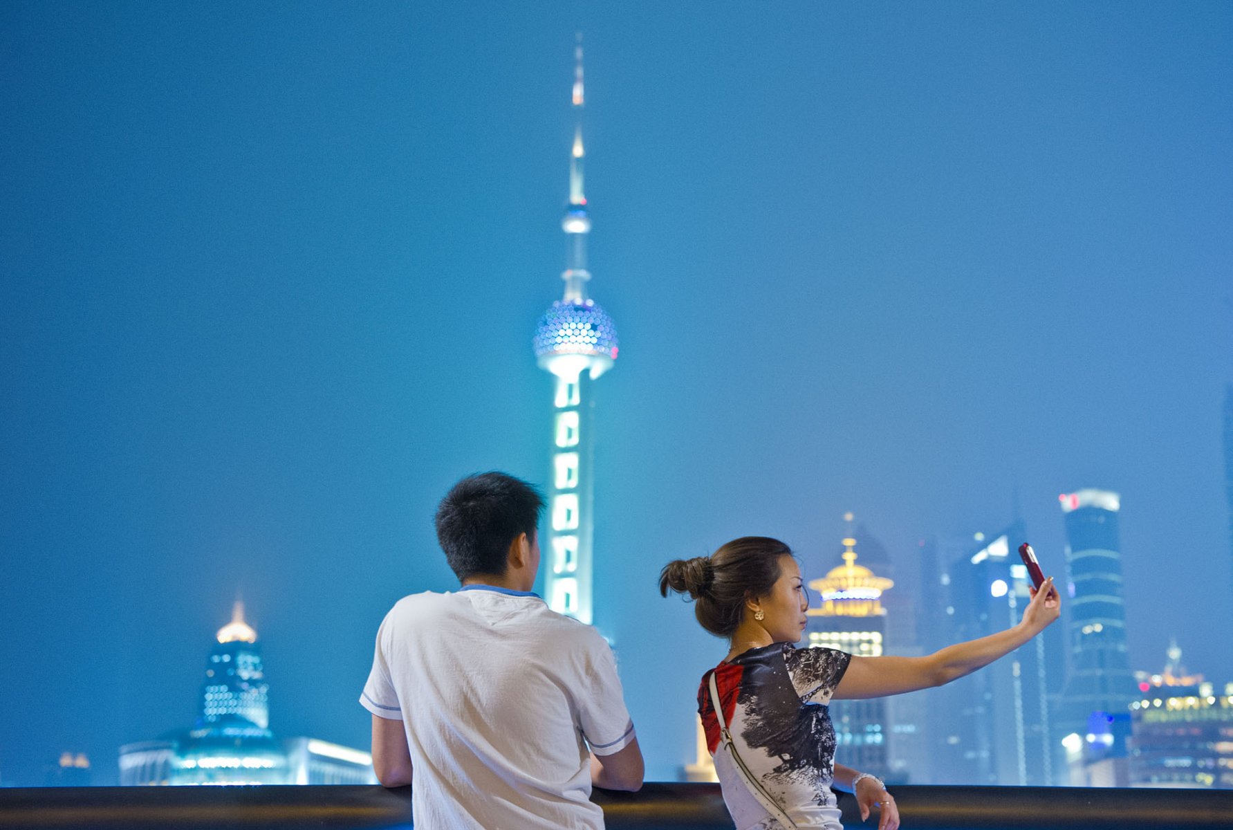 Mit ihrem Handy schiesst eine junge Chinesin ein Erinnerungsfoto, während ihr Begleiter die Aussicht auf die erleuchtete Skyline des Finanzdistrikts bevorzugt. Foto: Boris Roessler