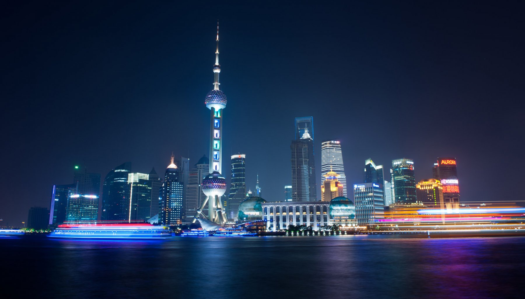 Bunt leuchten Ausflugsfähren, von denen aus die Passagiere einen Blick auf die illuminierte Skyline von Pudong werfen können. Foto: Boris Roessler