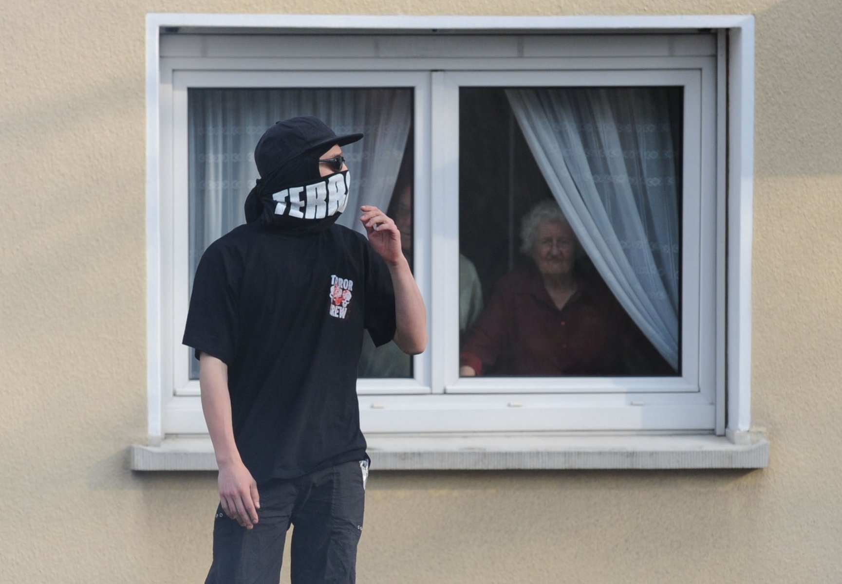 Ein vermummter Demonstrant steht in Straßburg vor einem Haus, aus dessen Fenster er von einer älteren Frau beobachtet wird. Foto: Boris Roessler dpa/lsw