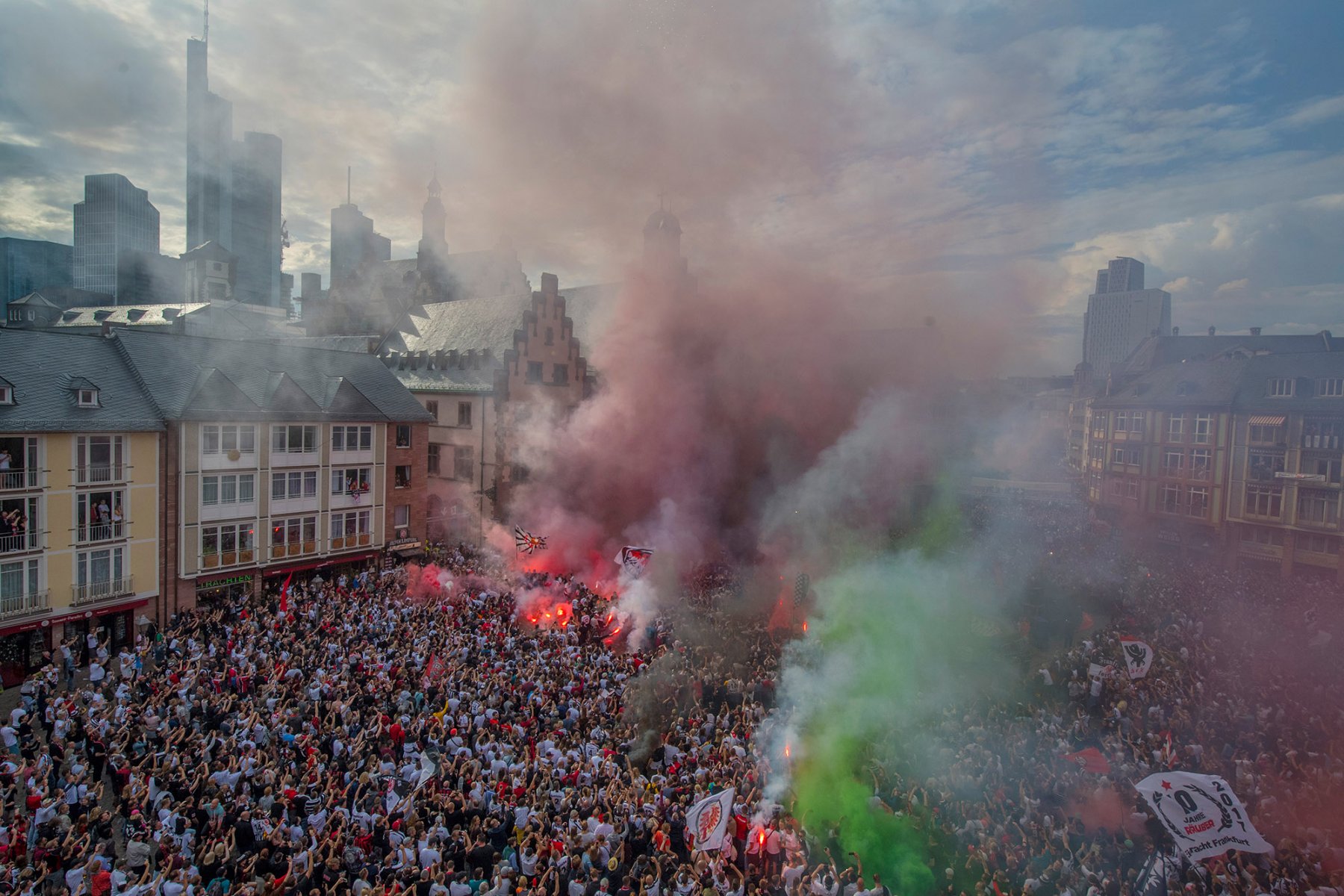Die Spieler von Eintracht Frankfurt feiern auf dem Römer-Balkon. Dabei brennen Fans Bengalos ab, deren Rauch die Sicht vernebelt. Foto: Boris Roessler/dpa