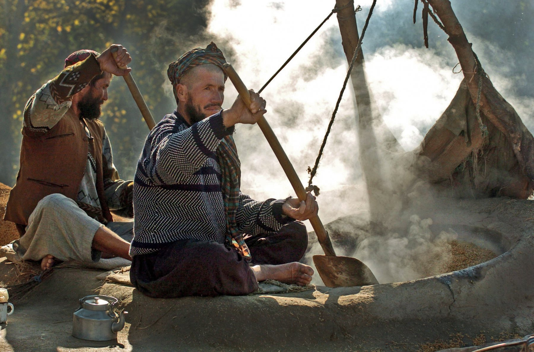 Two farmers dry the rice in two huge clay pans which are heated by an oven, in the province of Takar, Afghanistan. Photo: Boris Roessler/dpa