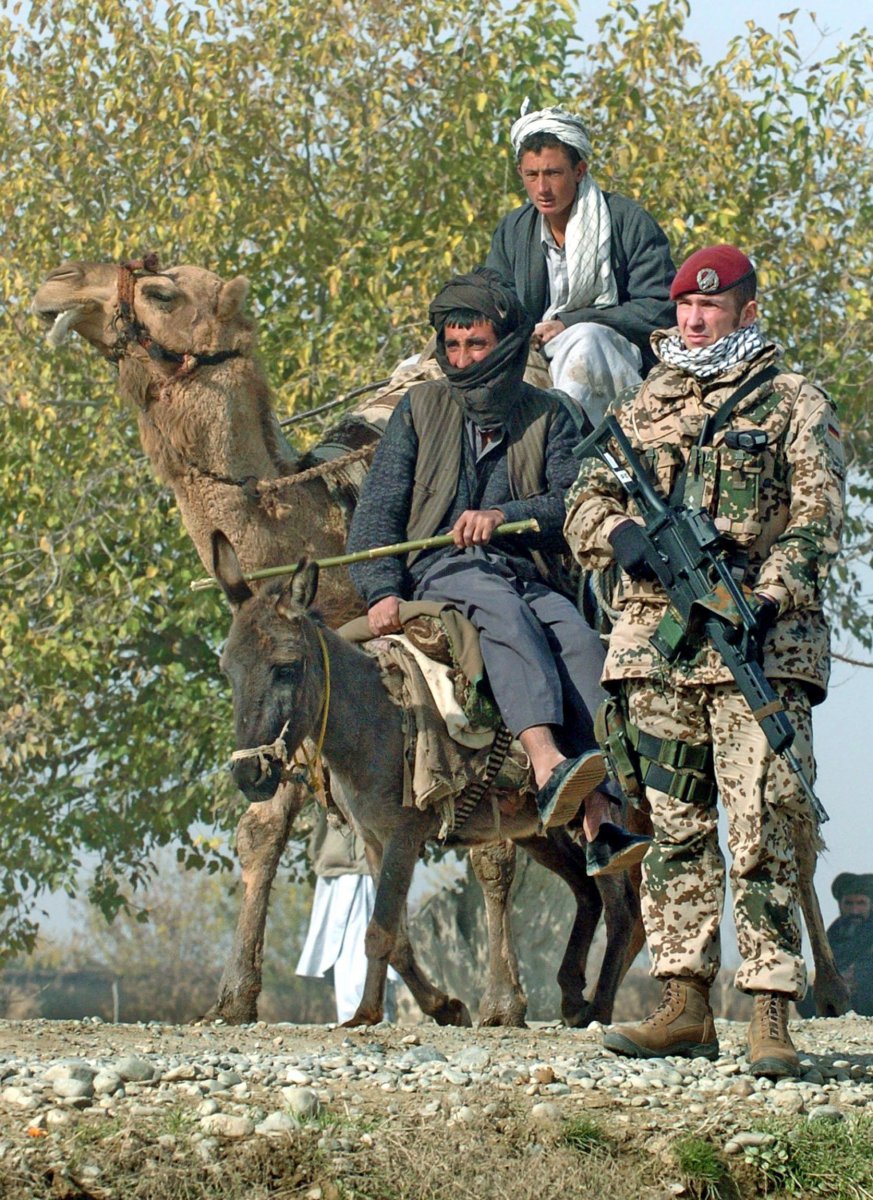 Afghan farmers riding on a camel and a donkey pass a German Bundeswehr soldier who guards a road near Kundus, Afghanistan. Photo: Boris Roessler/dpa