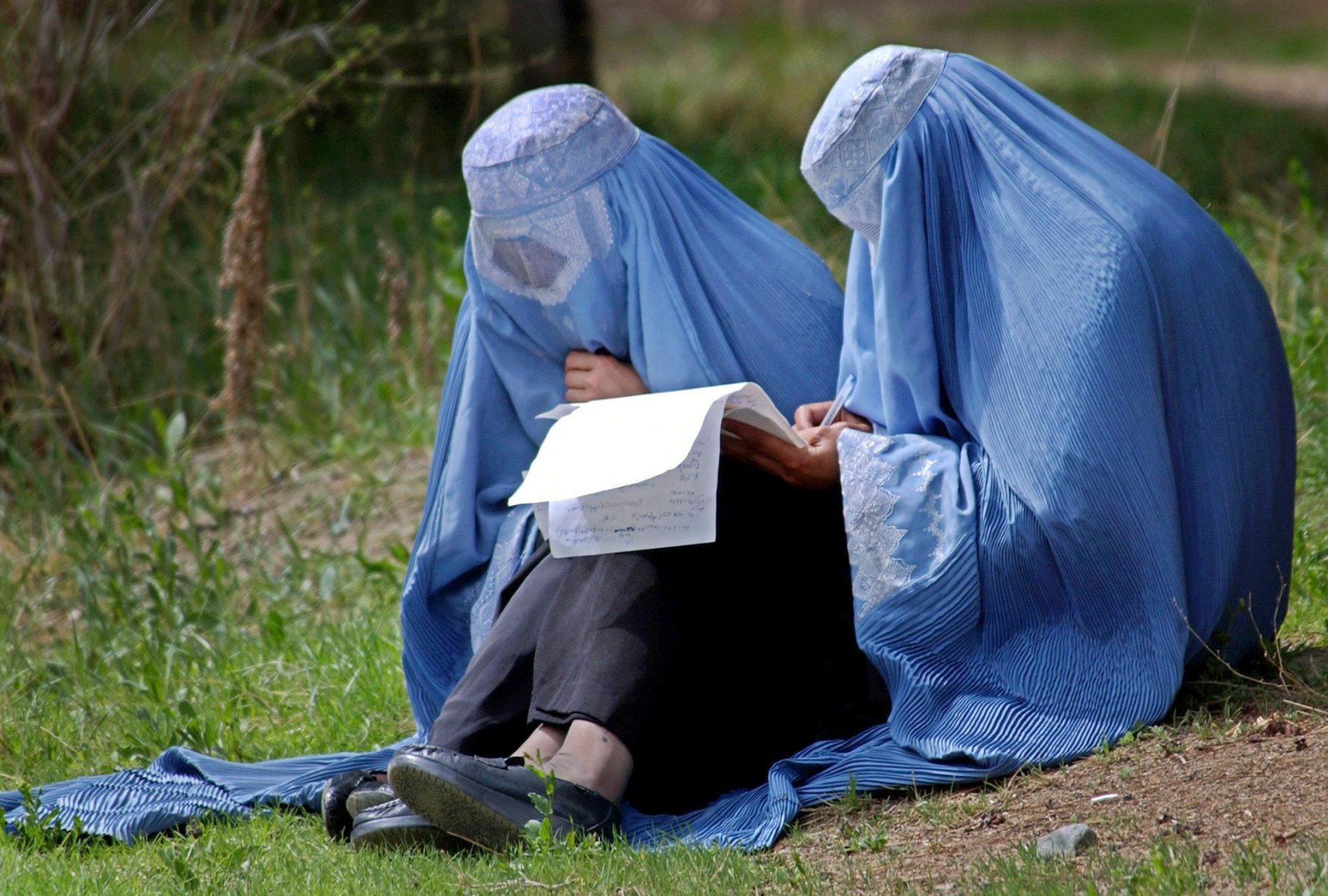 Veiled in traditional burqas two Afghan women sit on the campus of the university of Kabul and create their timetables for the upcoming Semester. For the first time since the Taliban regime, women were allowed to enroll again. Yet, many women still keep wearing the burqa, the long head-to-toe veil, even though it is no longer required. Photo: Boris Roessler/dpa