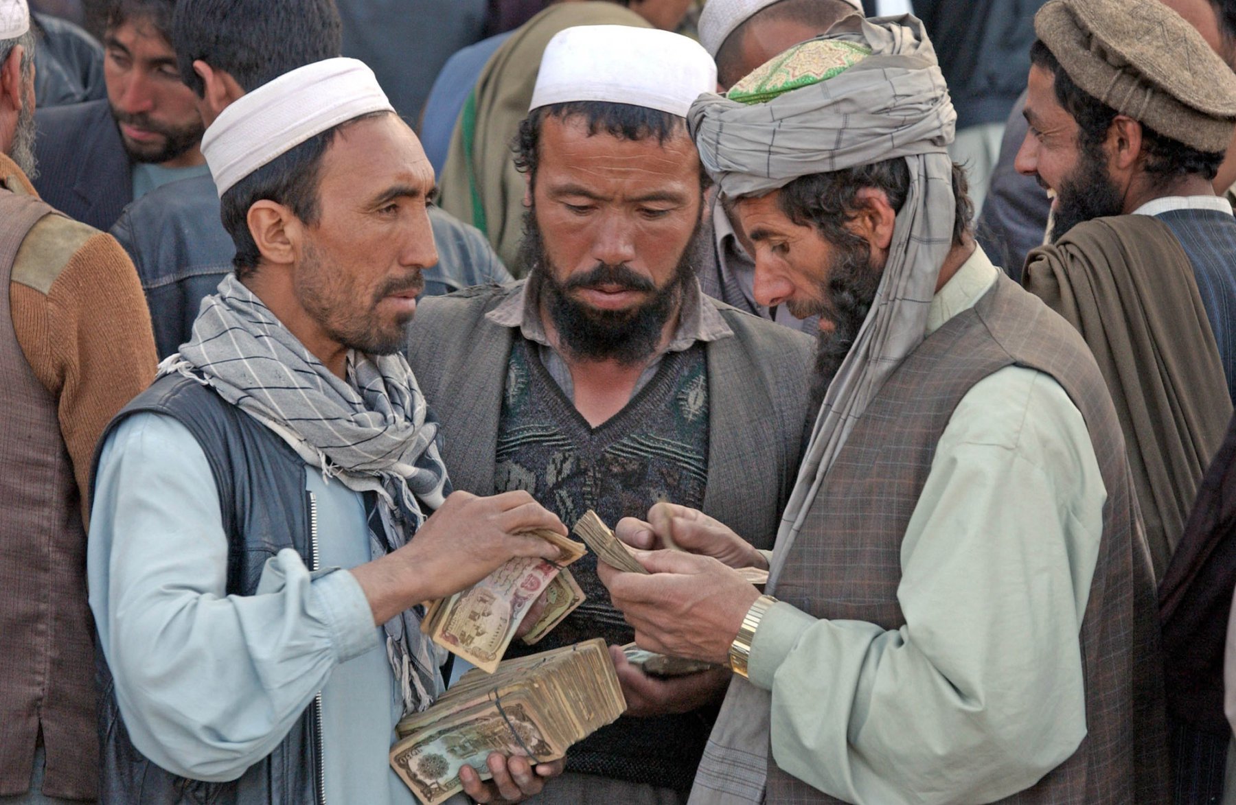 In eine geschäftliche Aktivität verwickelt sind drei Geldhändler, die auf einem Basar in Kabul bündelweise Afghani zählen. Für eine Dollar bekommt man derzeit rund 30.000 Afghani. Foto: Boris Roessler/dpa