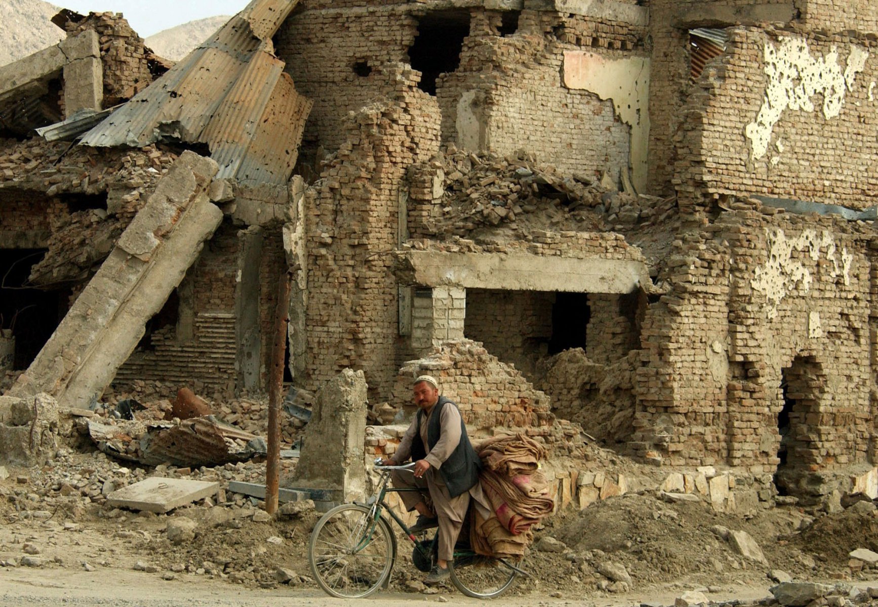 Mit einem Fahrrad fährt ein Mann an einer Hausruine im Universitätsviertel der afghanischen Haupstadt Kabul vorbei. Während große Teile der Stadt komplett zerstört sind, finden sich in manchen Bezirken kaum beschädigte Gebäude. Foto: Boris Roessler/dpa