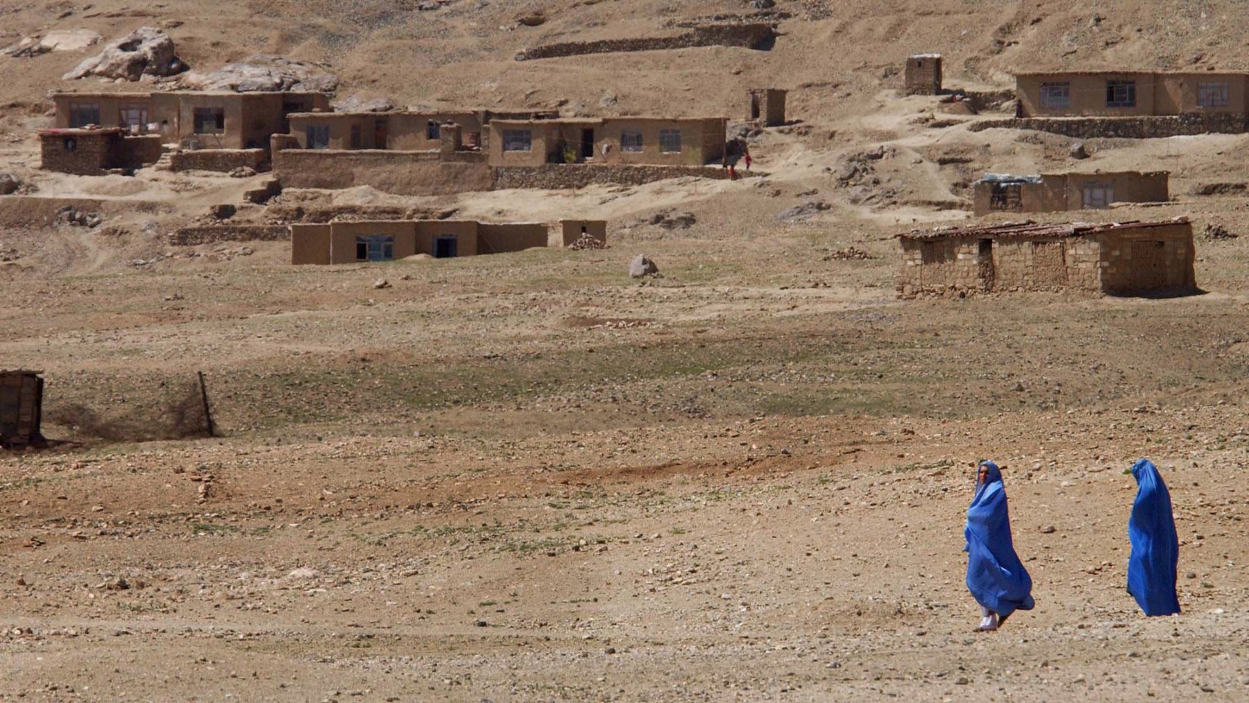 An Behausungen vorbei gehen zwei mit einer blauen Burka verschleierte afghanische Frauen am Donnerstag (28.03.2002) in Kabul. Viele Frauen tragen auch weiterhin das traditionelle Gewand. dpa